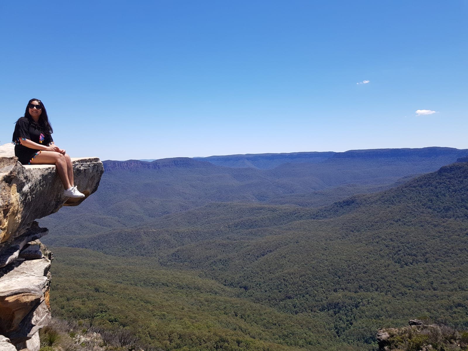 Palak sitting on a rock ledge above the forested valleys of the Blue Mountains