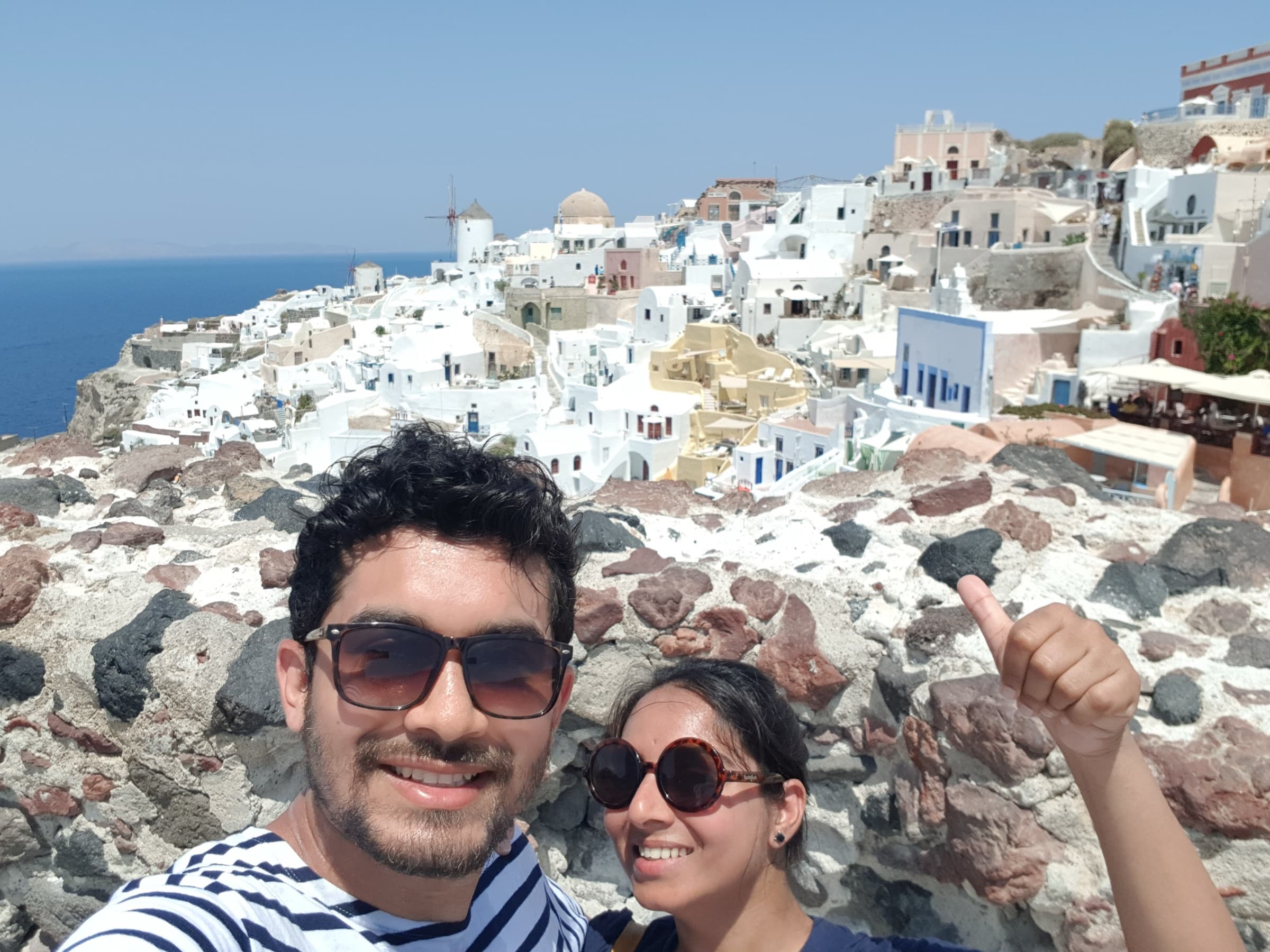 Palak and Pranav smiling in front of Oia's white houses and blue sea